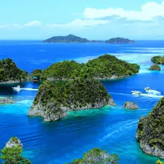 Rajska indonezyjska wyspa z turkusową wodą, bujną zielenią i łodziami sunącymi po falach.