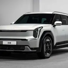 Biały, futurystyczny SUV Kia EV9 z charakterystycznymi światłami LED i masywnymi felgami stoi na szarym tle.
