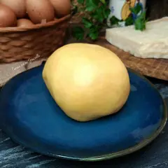 Impasto giallo per frolla salata su piatto blu, con uova e parmigiano sullo sfondo.