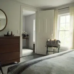 Ein runder **Spiegel im Schlafzimmer** hängt über einer Kommode. Ein Koffer steht bereit, die Tür ist offen.