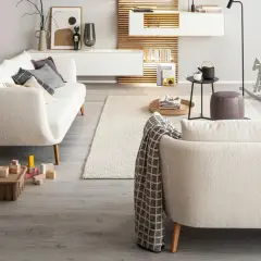 Gemütliches Wohnzimmer mit einem cremefarbenen Sofa vor bodentiefen Fenstern. Ein Kaminfeuer wärmt den Raum.