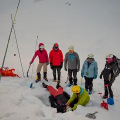 Ratownicy ćwiczą akcję ratunkową po lawinie w Tatrach. Jedna osoba zasypana, inni szukają jej w śniegu.