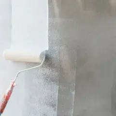 Rodillo aplicando imprimación blanca sobre pared gris. La imprimación prepara la superficie para la pintura.
