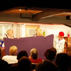 Schauspieler des losemund theater halten ein lila Tuch, während sie vor einem Publikum auftreten.