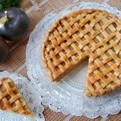 Tarta de manzana de la abuela, dorada y con un enrejado perfecto. Un trozo ya servido en un plato de cristal.
