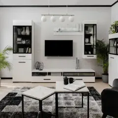 Nowoczesny salon czarno biały z meblościanką, telewizorem, stolikami i roślinami.