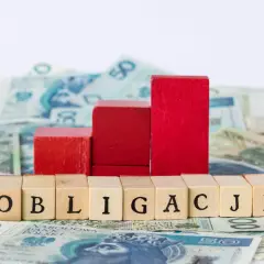 Drewniane klocki z napisem "OBLIGACJE" na tle polskich banknotów. Czerwone klocki tworzą wykres wzrostu.