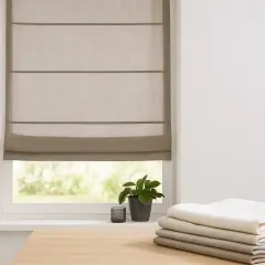 Ein beiger Raffrollo mit Vorhang kombinieren? Hier ist ein Beispiel: Ein schlichtes Raffrollo über einem Fenster, daneben ein Stapel Stoffe in verschiedenen Grautönen.