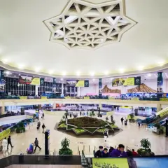 Wnętrze lotniska, które może być największym lotniskiem na świecie, z wielopoziomowymi galeriami, schodami ruchomymi i centralną zieloną przestrzenią.