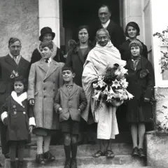 Mahatma Gandhi mit seiner Familie und Freunden, umgeben von Kindern, die Blumen halten.