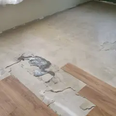 Il pavimento in PVC si solleva in più punti, mostrando il sottofondo danneggiato. Si vedono nuove doghe di legno pronte per la posa.