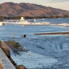 El espigón Garrucha bajo el agua, con olas rompiendo y montañas al fondo.