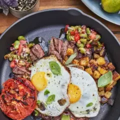 Un plat de petit-déjeuner copieux dans une poêle en fonte : steak grillé, deux œufs au plat, pommes de terre rôties, tomate grillée et une salade de légumes. Un vrai oeuf barbecue !