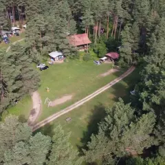 Malowniczy widok na stanicę wodną Zgon otoczoną lasem sosnowym. Widać domki, samochody i plac zabaw.