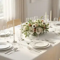 Un dressage de table simple avec des assiettes blanches, des verres à pied, des bougies et un centre de table floral.