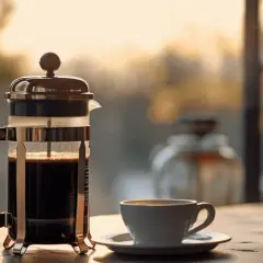 En brygga presskaffe står redo vid fönstret, med en kopp kaffe som väntar. Solen lyser genom glaset.