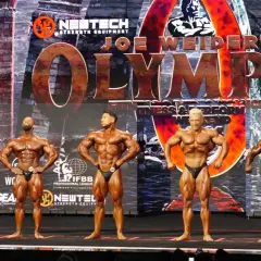 Fünf muskulöse Männer posieren auf der Bühne bei einem Bodybuilding-Wettkampf. Die "Joe Weider's Olympia" Bühne ist im Hintergrund zu sehen.