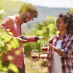 Coppia sorridente assapora il vino rosso Malenchini in un vigneto soleggiato.