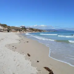 Arena dorada y aguas turquesas en la playa Remior, con algunas personas disfrutando del sol y el mar.