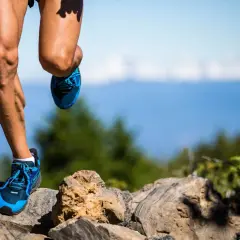 Nogi biegacza w niebieskich butach na kamienistym szlaku, przygotowującego się do ultramaratonu. Ile km? Tego nie wiemy, ale wysiłek jest widoczny.