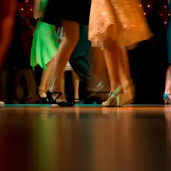 Nogi w ruchu, błyszczące sukienki i eleganckie buty. Wszyscy tańczą, tworząc dynamiczny obraz, jakby to był belgijka taniec.