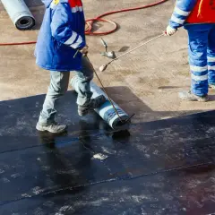 Arbeiter verlegen schwarzes Flachdach Material mit einer Rolle und einem Brenner.