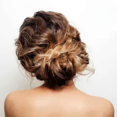 Un elegante recogido alto con pelo rizado y un detalle de trenza rubia.