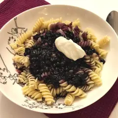 Fusilli z jagodami i kleksem śmietany na talerzu z czarnymi wzorami.