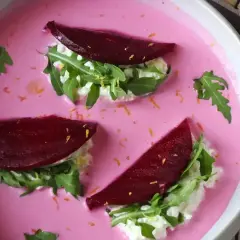 Vacker vegetarisk mat: rödbetor, ruccola och färskost i en rosa soppa, garnerad med rivet citronskal.