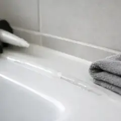Pistolet do silikonu i szara ściereczka obok świeżo nałożonej spoiny. Czekamy, aż silikon schnie.