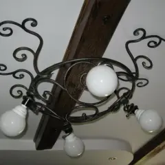 Elegantes lámparas de forja de techo con volutas y globos de cristal blanco, adornando un techo con vigas de madera.