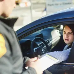 Policjant wręcza kobiecie w samochodzie dokumenty. Wygląda na to, że chodzi o mandaty w Austrii.