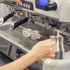 Mano che prepara un caffè con la bar macchina caffè. Due tazzine bianche attendono il loro turno.