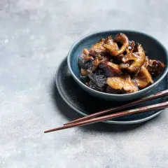 Deliciosas setas shiitake salteadas en un cuenco azul, listas para ser disfrutadas con palillos.