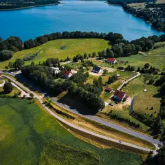 Malownicze **trasy rowerowe Mazury** wiodą przez zielone pola i lasy, w pobliżu błękitnego jeziora.