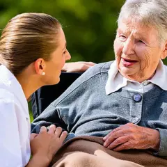 Pflegekraft spricht einfühlsam mit älterer Dame, Validation Demenz im Fokus.