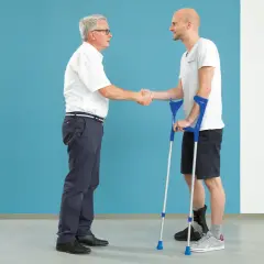 Arzt schüttelt Hand eines Patienten mit Krücken und Orthese am Fuß nach einer Calcaneusfraktur.