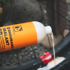Pouring orange Endurance Sealant into a bike tire. This sealant is designed for longer-lasting protection compared to regular options.