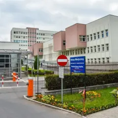 Nowoczesny budynek szpitala z bramkami wjazdowymi i znakami informacyjnymi.