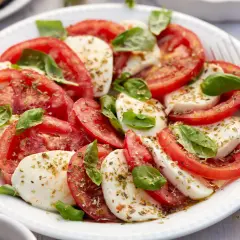 Ensalada caprese fresca con rodajas de tomate y mozzarella, aderezada con albahaca y especias.