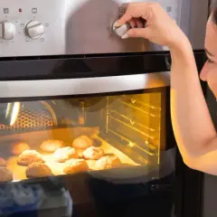 Kobieta ustawia temperaturę piekarnika, zastanawiając się, ile prądu zużywa piekarnik podczas pieczenia ciasteczek.