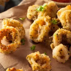 Anelli dorati e croccanti di calamari gratinati al forno, guarniti con prezzemolo fresco e accompagnati da una salsa rossa.
