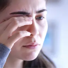 Kobieta zamyka oko, jakby odczuwała ból lub miała zaćmę pourazową.