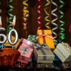 Uroczy tort z cyframi "60" i płonącymi świecami, otoczony prezentami i serpentynami. Idealne życzenia na 60 urodziny!