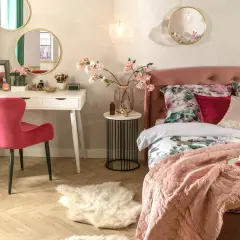Elegancka toaletka w sypialni z różowym krzesłem, lustrami i kwiatami.