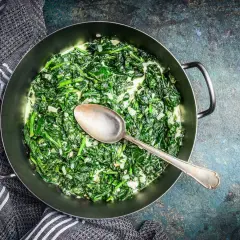Un plat réconfortant d'épinards à la crème, servi dans une poêle avec une cuillère.