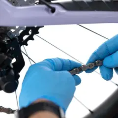 Ręce w niebieskich rękawiczkach sprawdzają kierunek łańcucha rowerowego przed jego montażem.