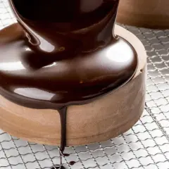 Un glaçage chocolat brillant et onctueux recouvre un petit gâteau rond, coulant sur les côtés.