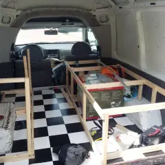 Wnętrze vana przerabiane na minicamper. Drewniana konstrukcja łóżka, szachownica na podłodze, skrzynka narzędziowa.