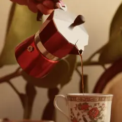 Czerwona kawiarka nalewa aromatyczną kawę do ozdobnej filiżanki. Idealna ilość kawy do kawiarki to klucz do porannego rytuału.